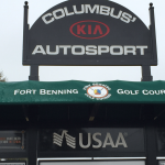 A close up picture of a black advertisement board, green awning over a golf scoreboard.