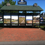 A golf course scoreboard with green tile roof and five panel advertisements