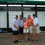 men and women stand in front of a golf scoreboard