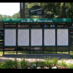 A golf scoreboard behind an area of landscaping on a golf course