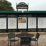 A set of black outdoor tables and chairs in front of a golf scoreboard.